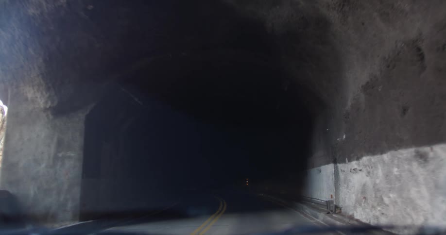 Vehicle enters dark tunnel through mountain encountering headlights from another vehicle