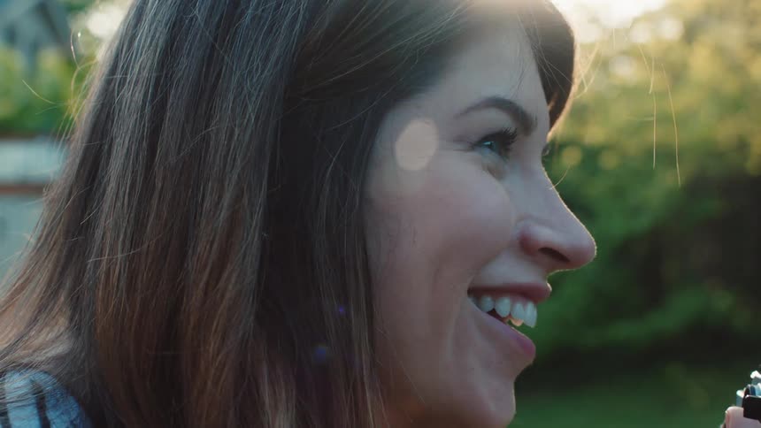 Female holding a camera smiles while bringing a camera up close to her face as she prepares to take a picture