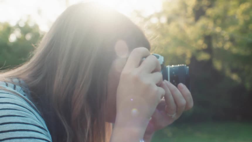 A woman holds a camera to her face and adjusts the focus