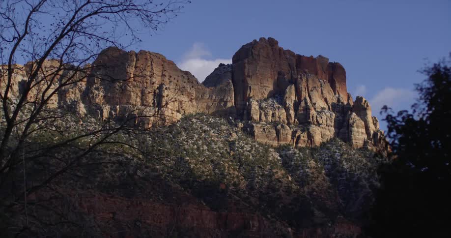 Tall butte with slope dotted by vegetation stands near road