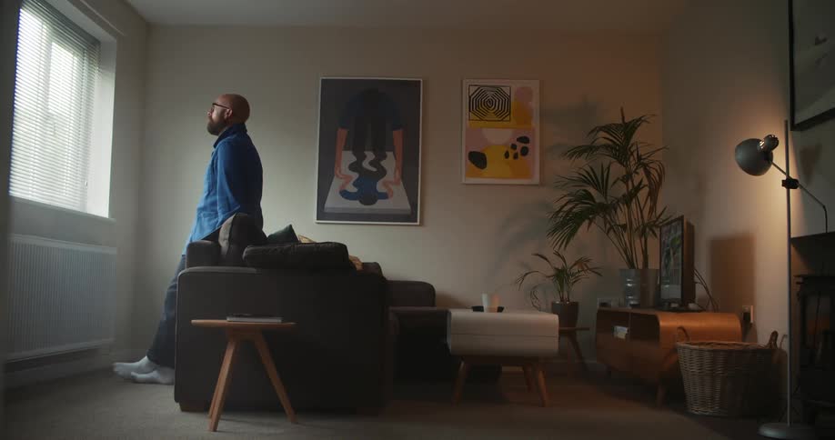 A man leans against his couch and looks out the window