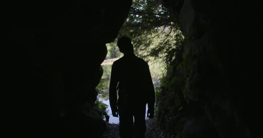 A man walks out of a cave towards a river