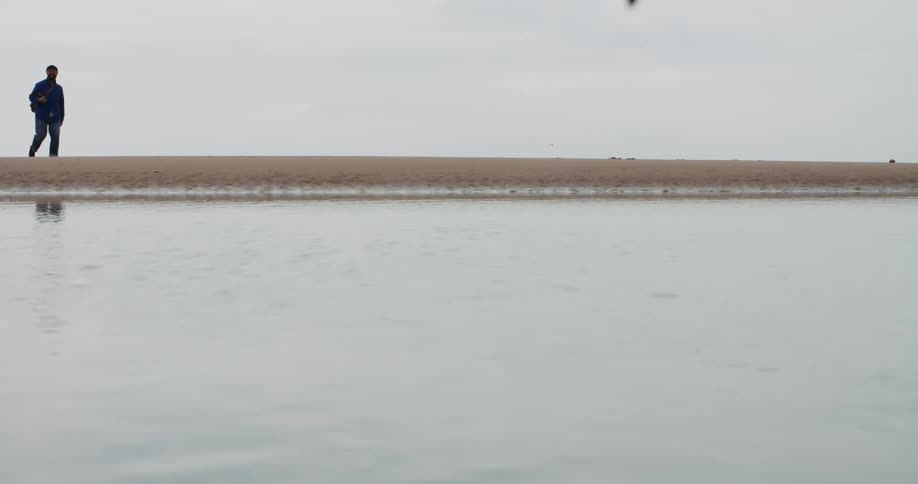 A man walks across the sand by the water