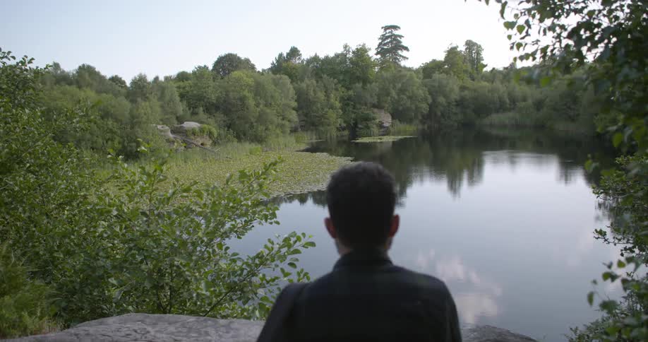 A white man stands and takes in a pond and trees in nature