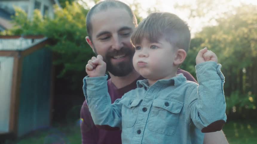 A father holds onto his sons waist as they play in their backyard