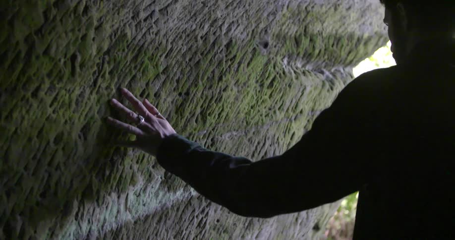 A man walks through a cave and touches the wall