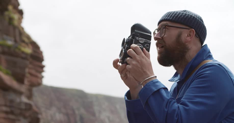 A man stands outdoors taking a photograph with a camera