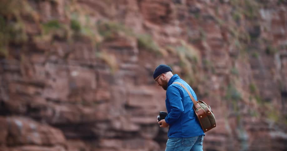 A photographer takes a picture of an escarpment before lowering his camera and walking off frame