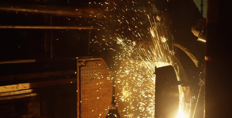 A person works on welding in the dark basement