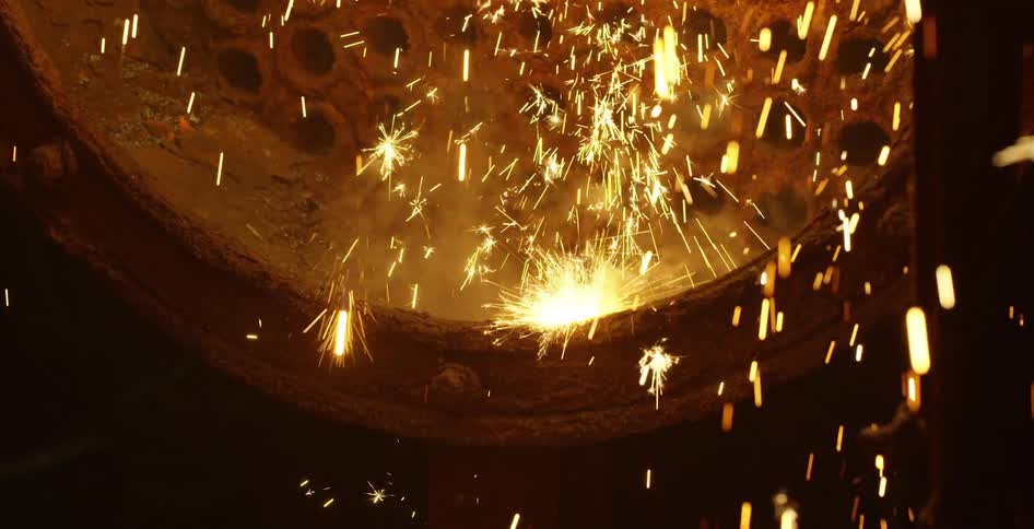 Sparks fall onto a rusted metal drum with holes