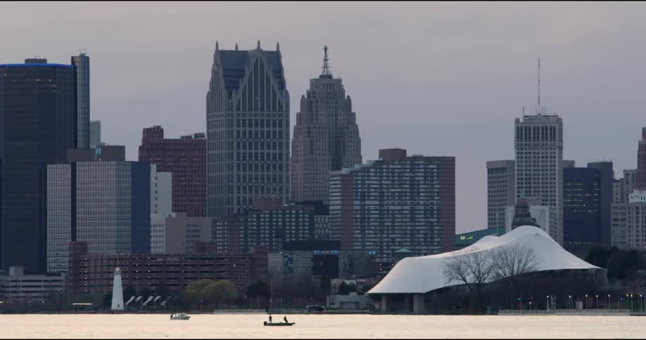 Two people stand in a kayak in a lake in front of a downtown city