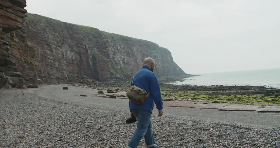 A man walking on a beach with the ocean and a cliff in the foreground