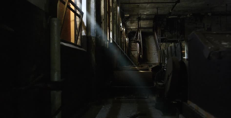 Ray of sunlight shines through window of factory full of grimy stored machines and metal parts
