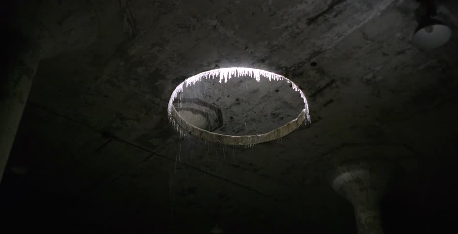 Icicles hang from a hole in a ceiling and rain falls in