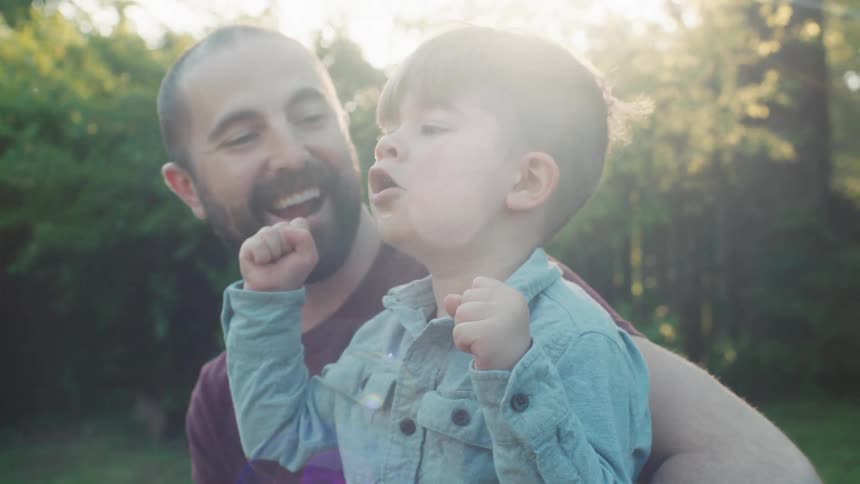 Father holds his son and laughs together in the garden