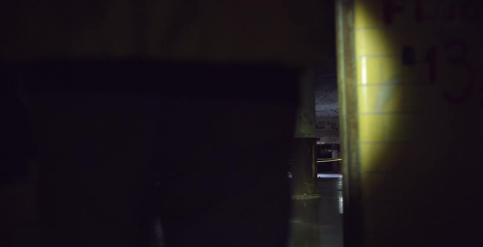 Person walks out of graffiti dotted tiled room onto openwalled building floor at night