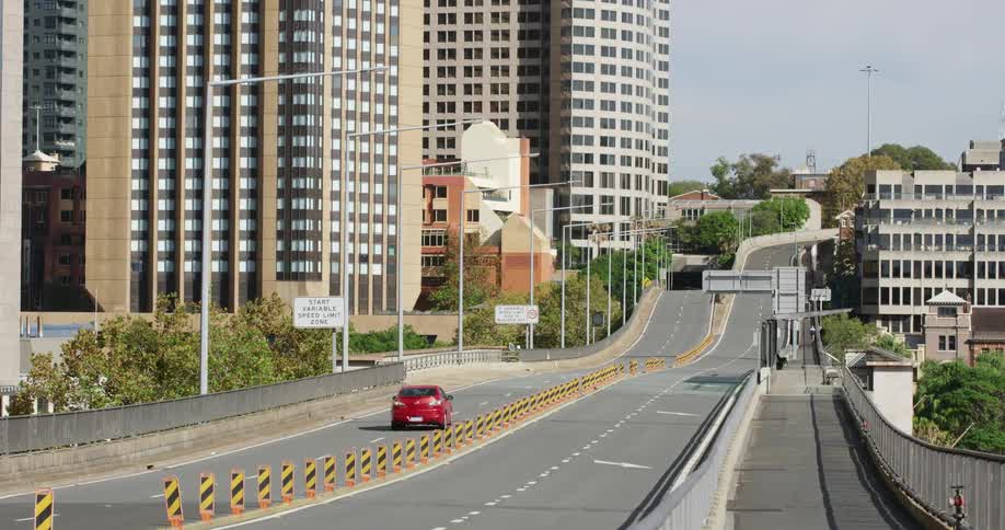 Single red car drives on an empty highway through the city