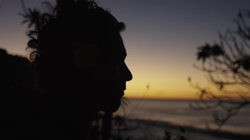 A teenager on a beach moves his head to a beat