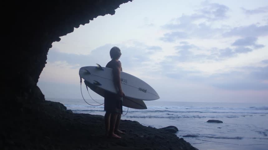 Two people stand on the shore holding their surfboards
