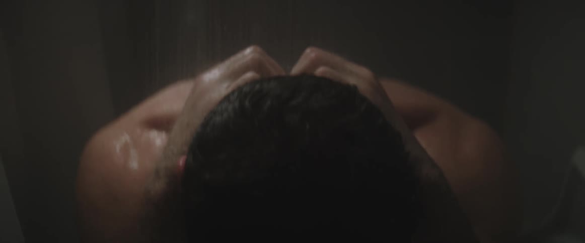A man is showering and touching his neck and head