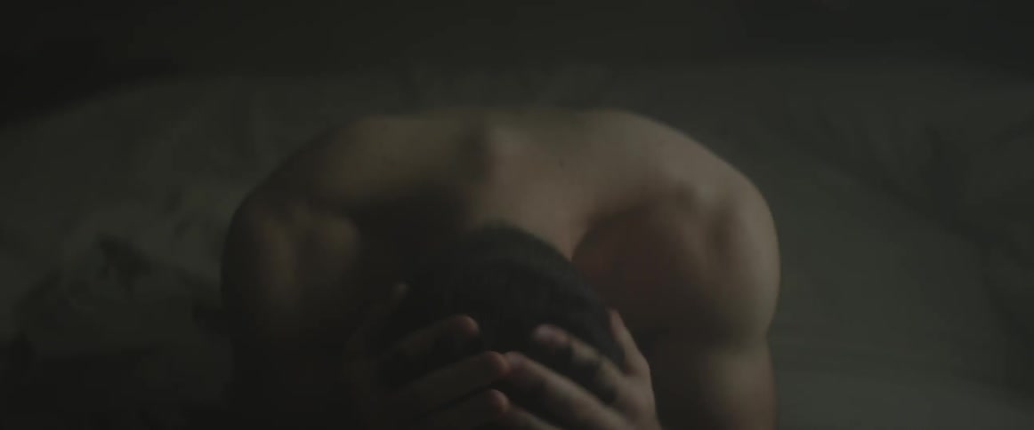 A man sitting on the edge of his bed running his hands through his hair