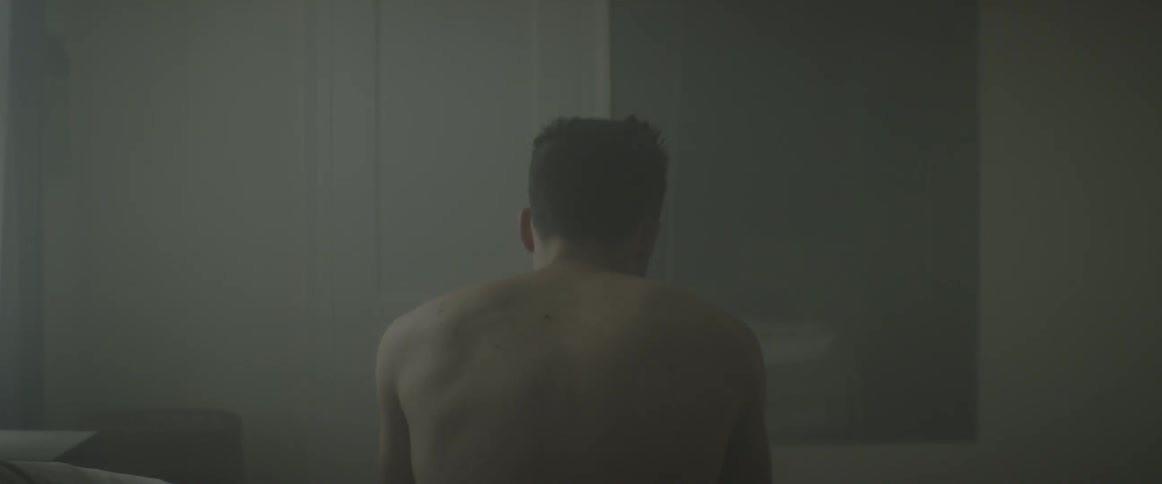 A shirtless man sitting on the edge of a bed