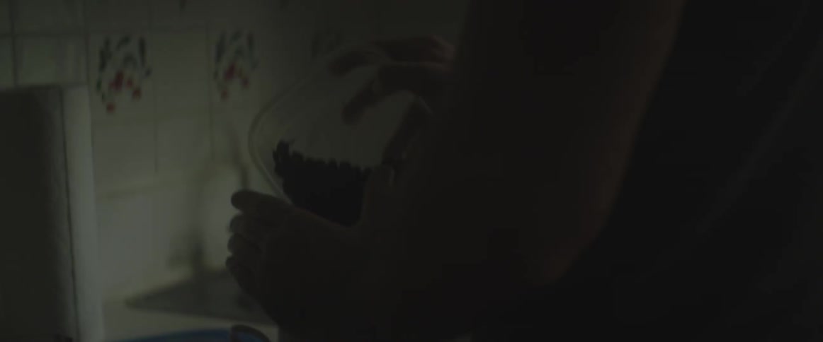 A man standing in a dimly lit kitchen pours coffee beans into a grinder