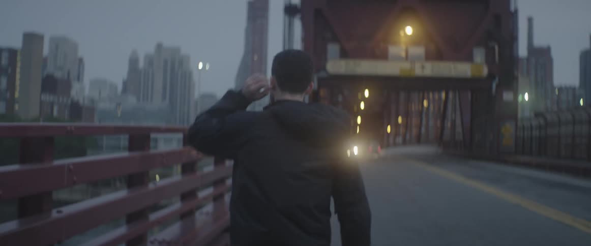 A man is walking across a bridge towards a city at sunset