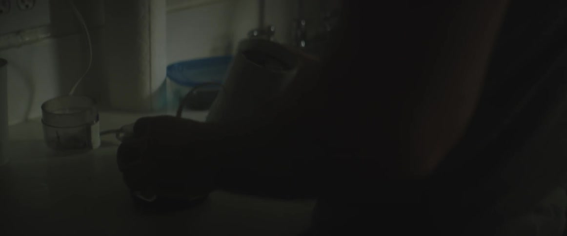 A man standing in a dimly lit kitchen pours coffee grounds out of a grinder
