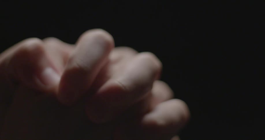 Hands and fingers tightly clasping against a black background