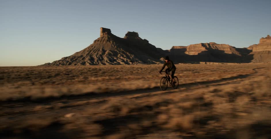 A cyclist riding down a dirt path through the badlands away from barren mountains