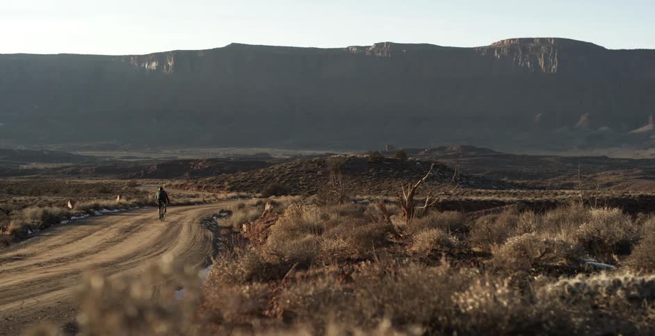 A man cycles down a dirt road towards a canyon