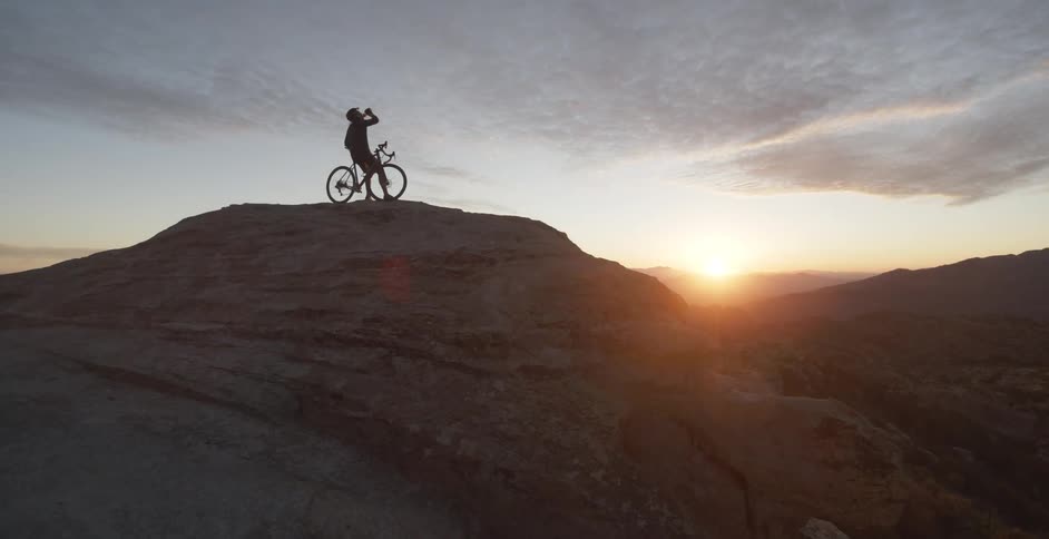 A person sits on a bicycle atop a high mountain cliff