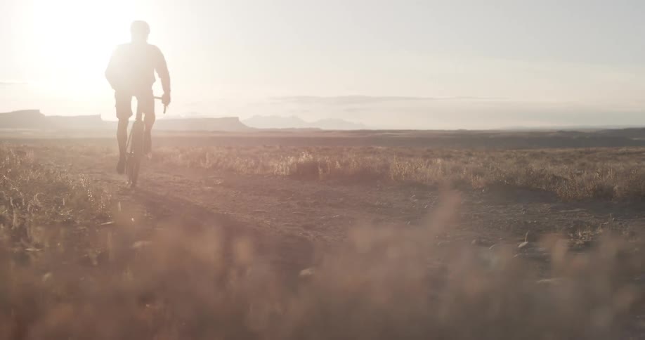 A person riding a bike in the desert with the sun and the sky in the background