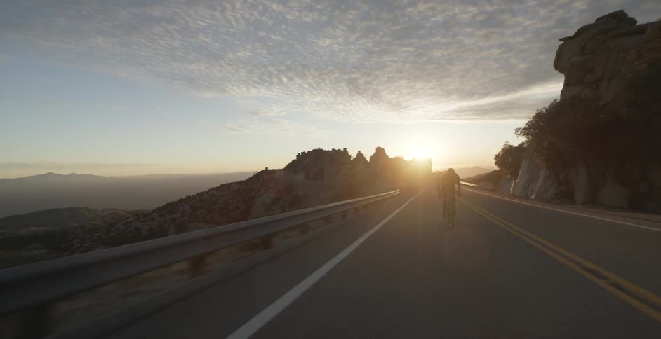 Male cyclist rides a bike on a mountain road at sunset