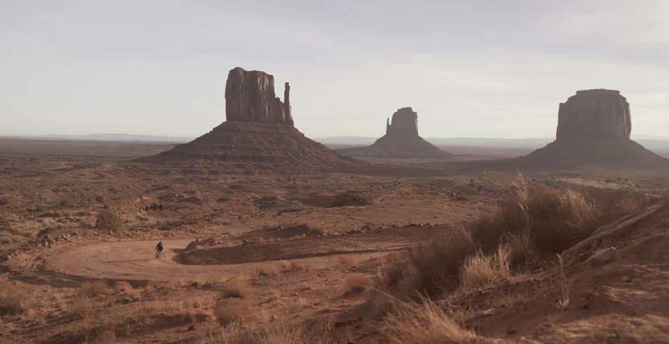 A cyclist riding a bicycle around a curved dirt road through monument valley