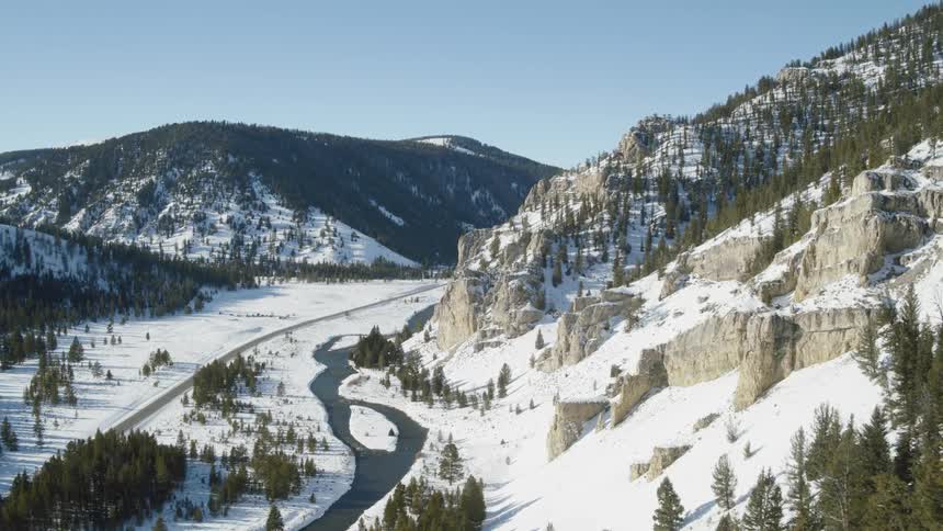 A stream winds and curves through the snow at the base of a mountain slope