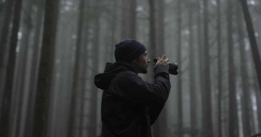 Male photographer takes a picture of the trees in the forest