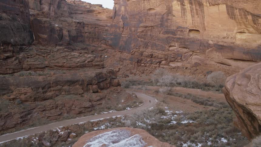 A bicyclist rides down a road that snakes through a rocky canyon