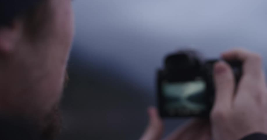 A man holding a camera with a lake and mountains in the background