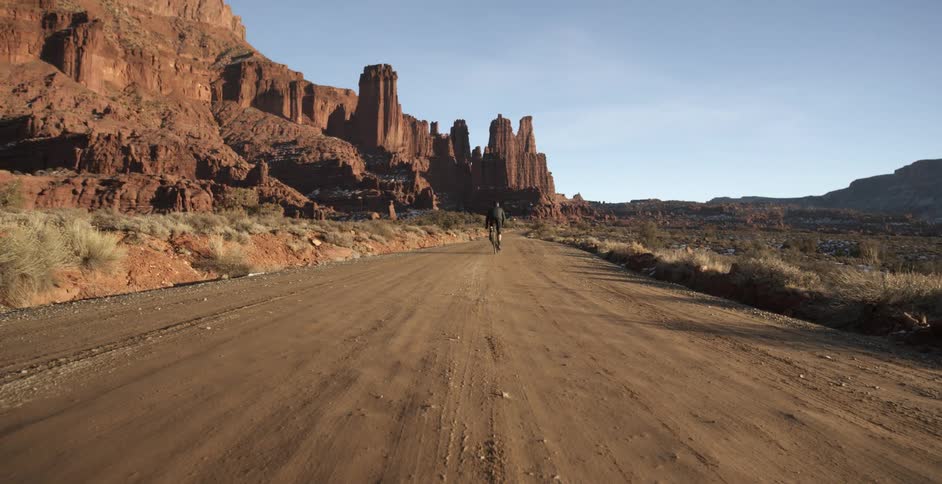 A man is biking in a desert area on a dirt road