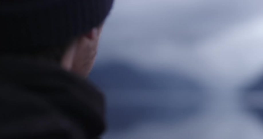 A man using a camera to take a photograph of foggy mountains looming over a lake on a cloudy day