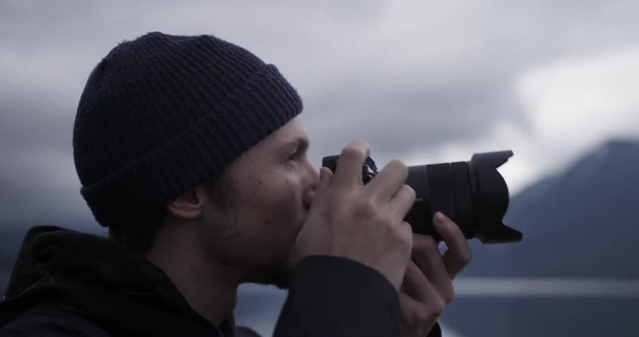 A man with a camera with a lake and mountains in the background