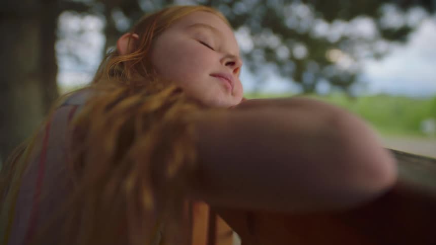 A young girl leaning on a railing with head on her arms opens her eyes