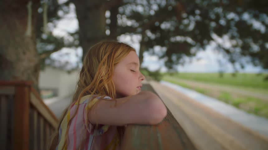A young girl leans on a railing with her eyes closed