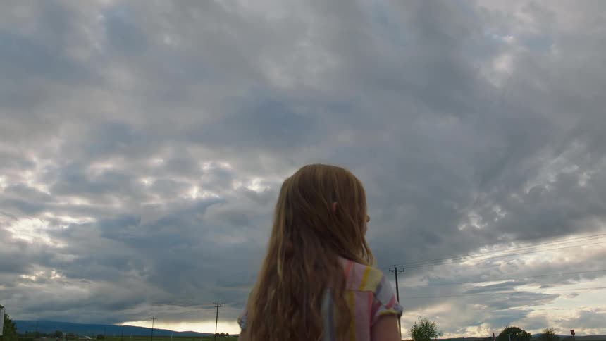 A young girl watches the sunset as clouds cover the sky