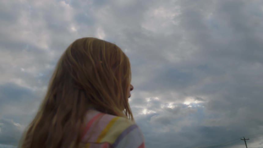 Little girl stands and looks around on a cloudy day in the field