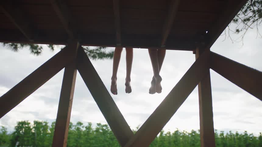 Two girls dangle their feet and legs off of a wooden platform