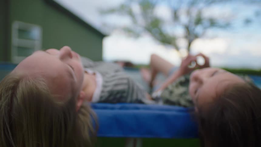 Two girls lay on a trampoline talking and laughing with each other