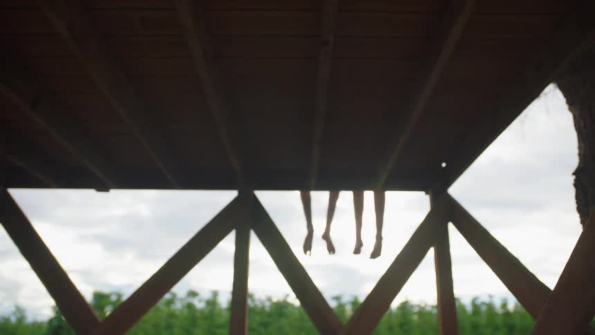 Two people sit on a dock with their legs dangling